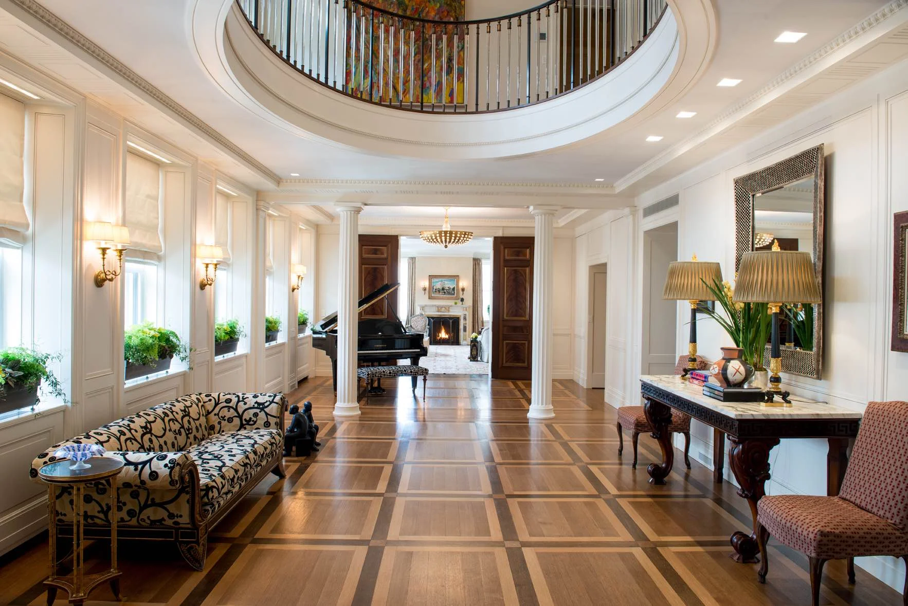 Luxurious foyer with curved staircase, hardwood floors, white paneling, and classical columns