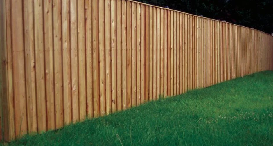 Newly installed cedar vertical board privacy fence along manicured lawn at dusk