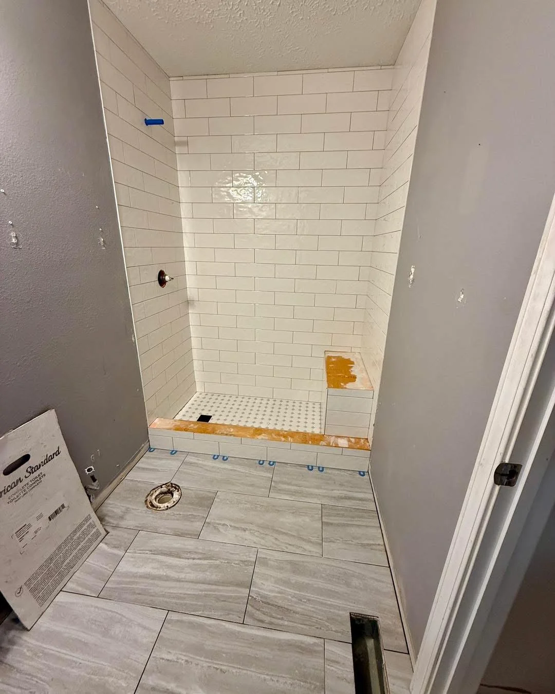 Newly tiled shower enclosure with white subway tiles and wood-look floor tiles during construction