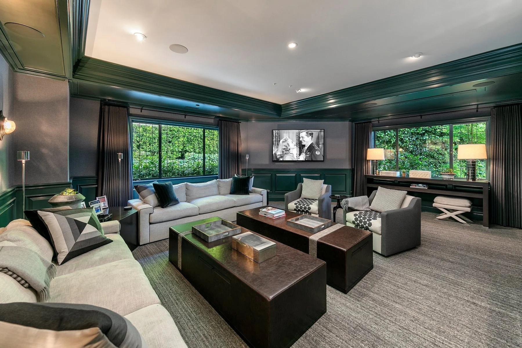 Luxury media room with green millwork, gray upholstered seating, and dark wood tables