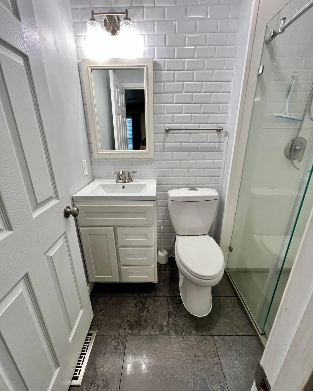 Modern bathroom with white subway tile walls, vanity sink, toilet, and glass shower enclosure