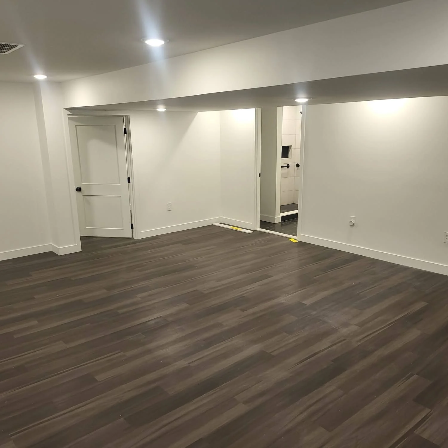 Finished basement with dark vinyl plank flooring, white drywall, recessed lighting, and white trim doors