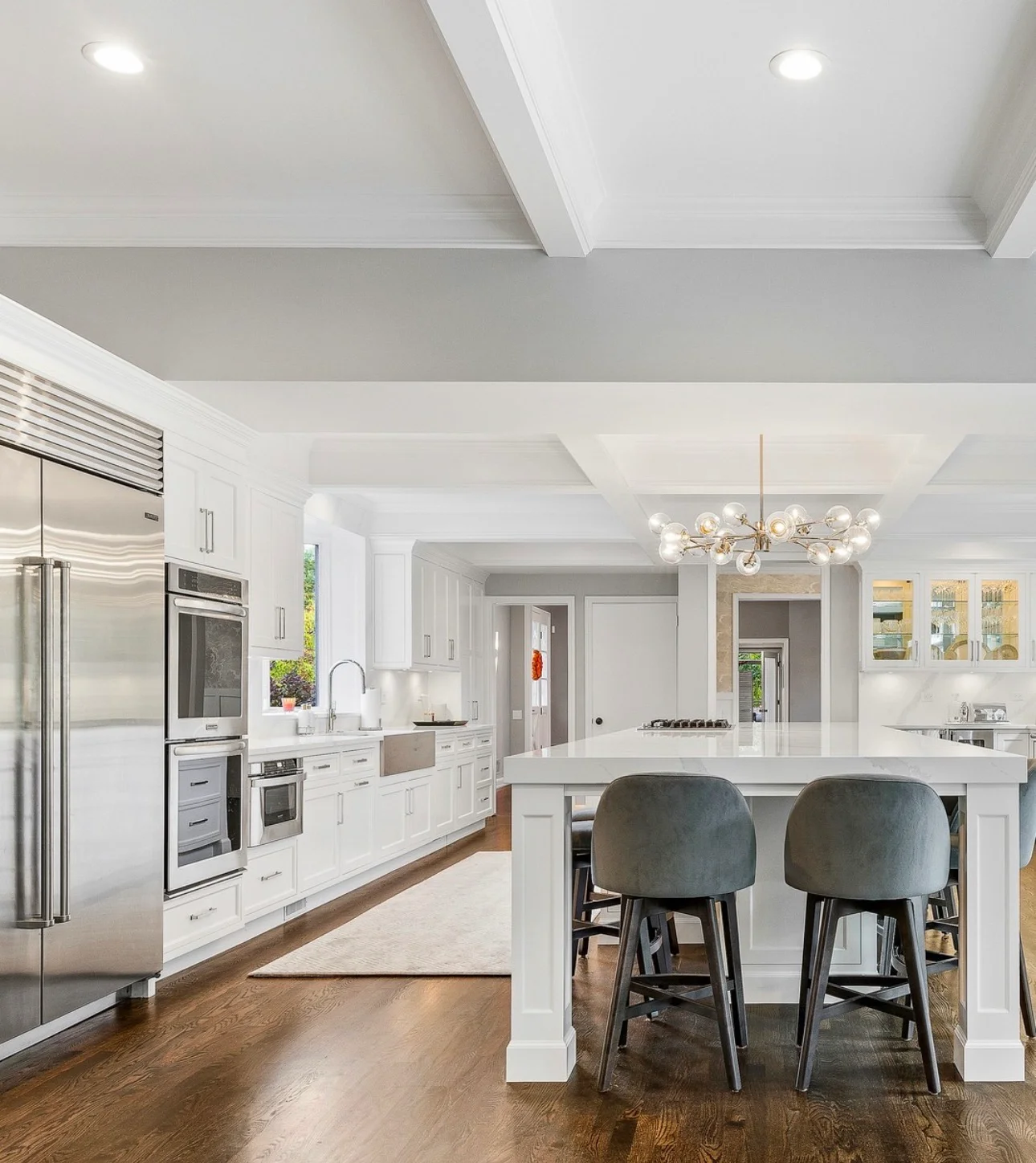 Modern white kitchen with island, stainless appliances, and coffered ceiling