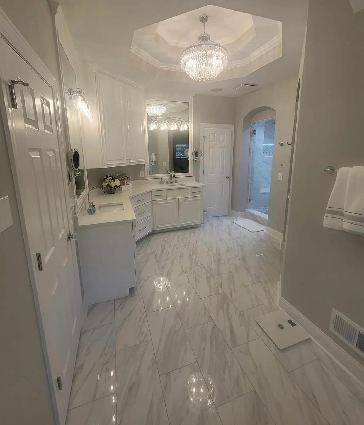 Bright white master bathroom with marble floors, white cabinetry, and crystal chandelier