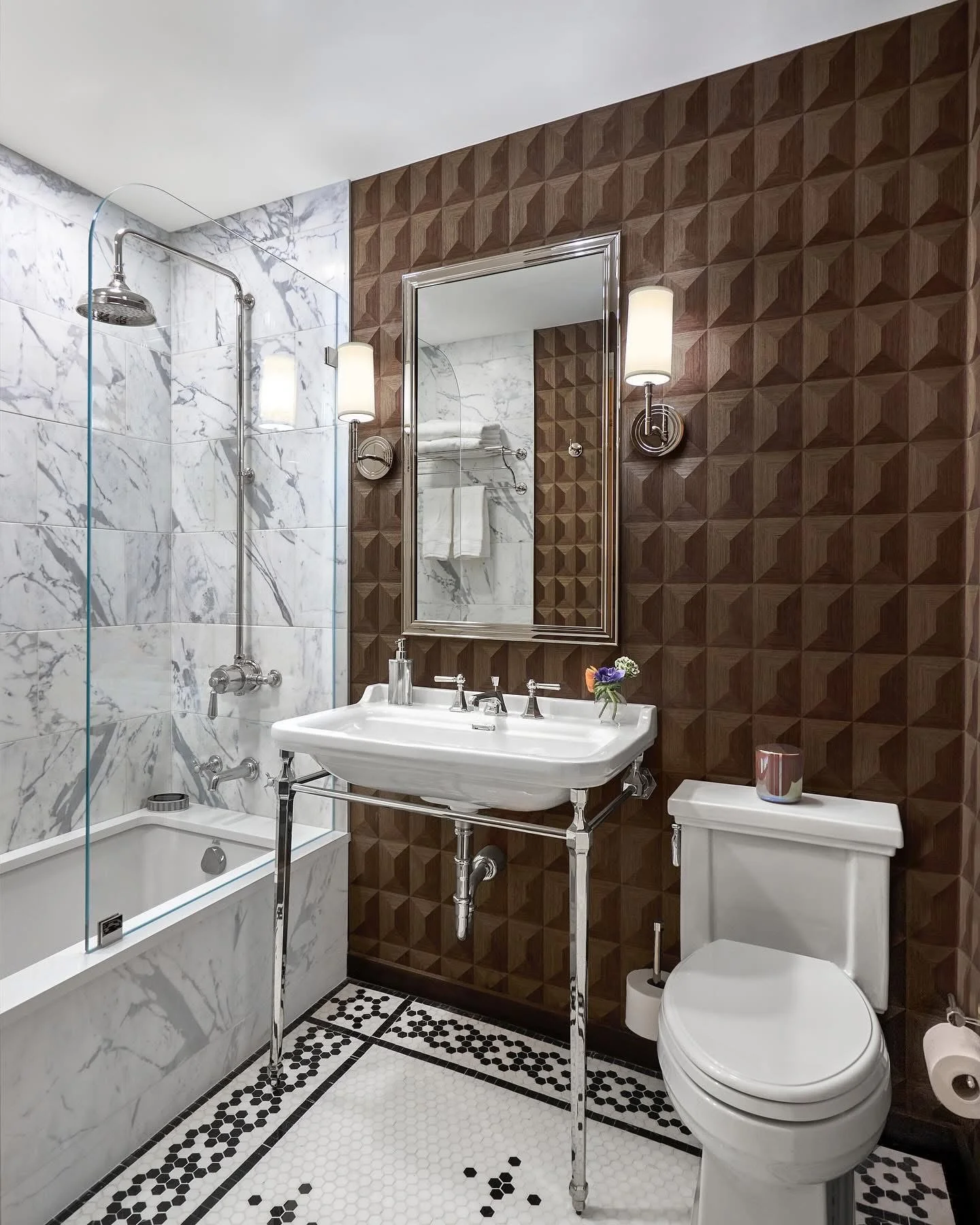 Luxury bathroom with marble shower, brown geometric walls, pedestal sink, and black-white tile floor
