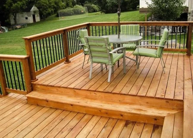 Large wooden deck with green patio furniture and black metal railings overlooking lawn