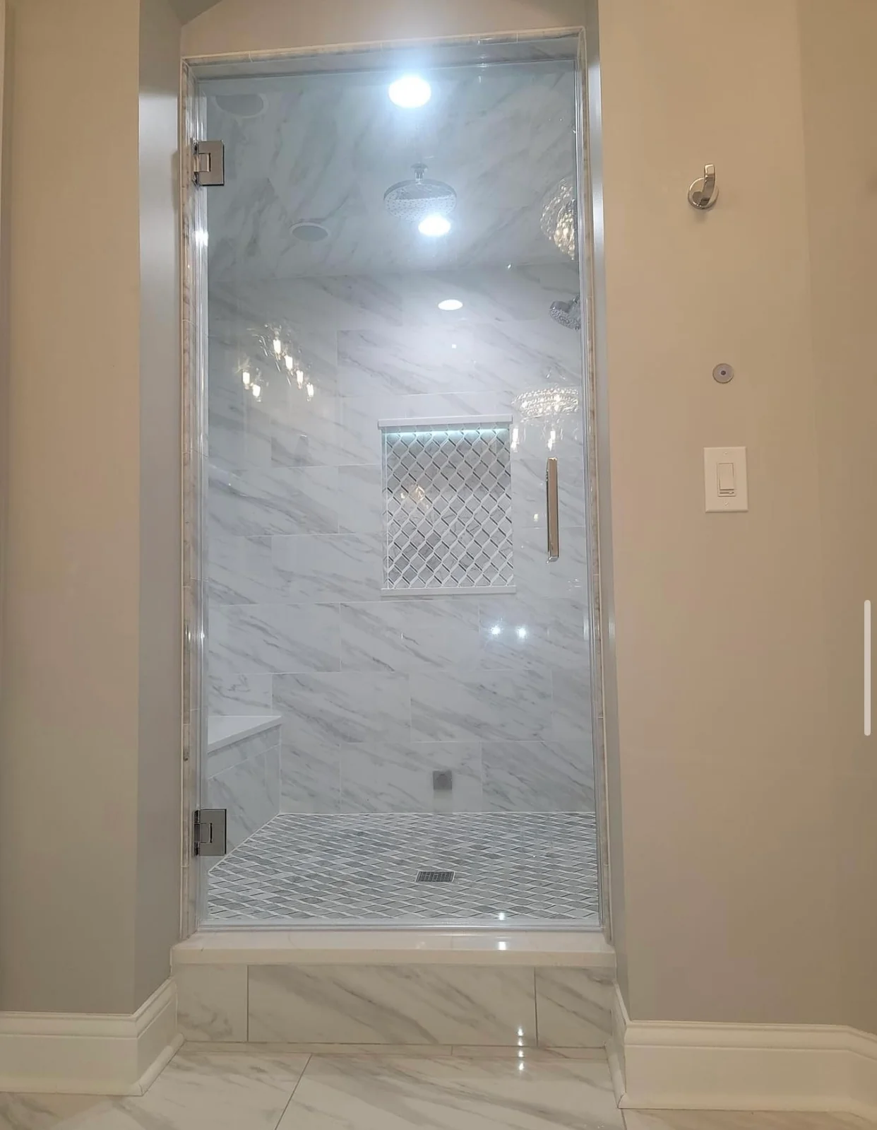 Frameless glass shower with marble tile walls and diamond mosaic accent panel
