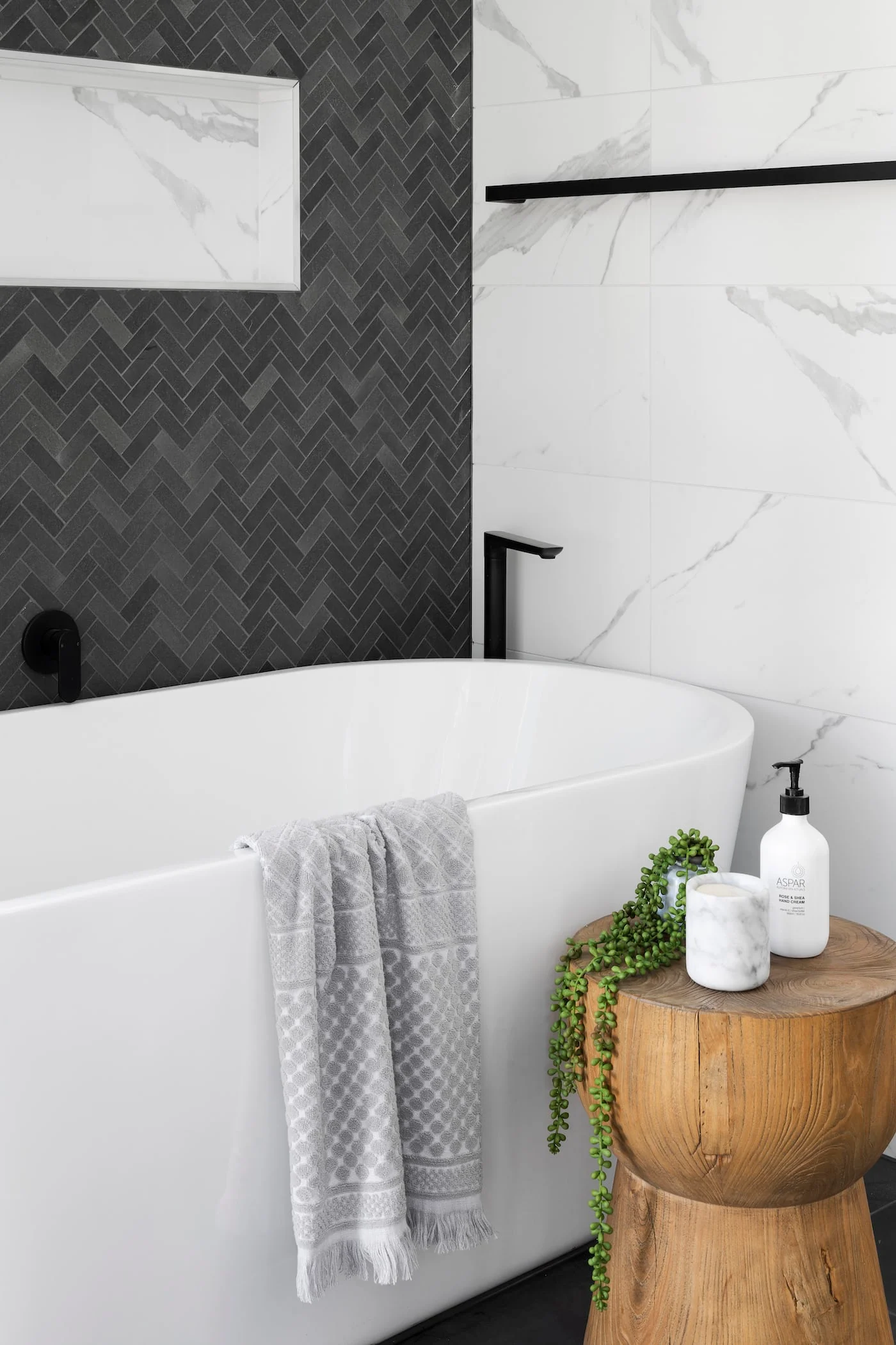 Modern bathroom with freestanding tub, herringbone tile accent wall, and marble finishes