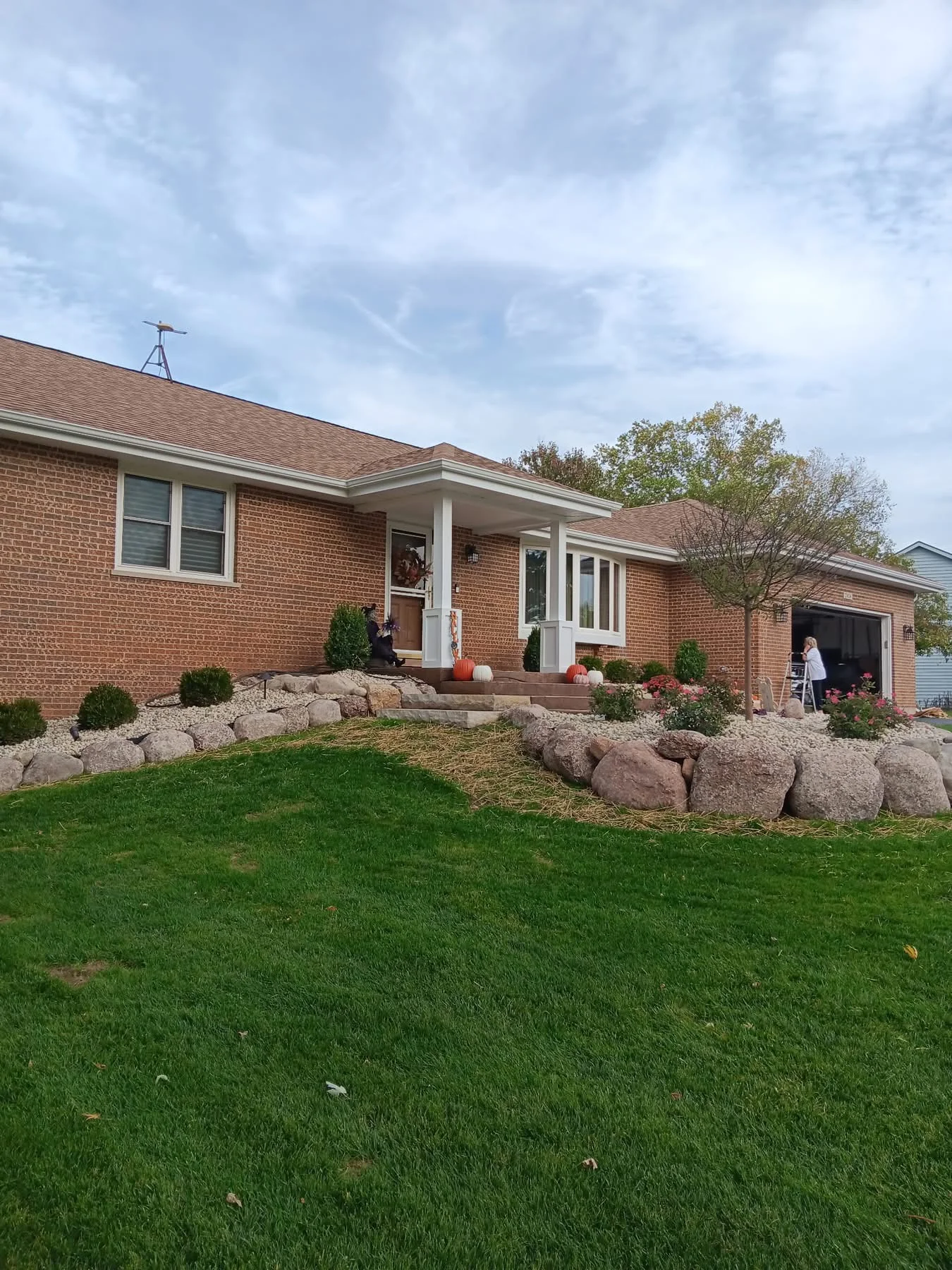 Brick ranch home with new white column portico, boulder landscaping, and green lawn