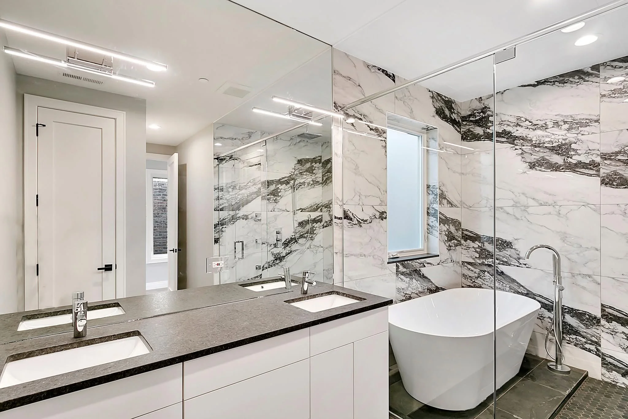 Modern bathroom with marble walls, freestanding tub, and frameless glass shower enclosure