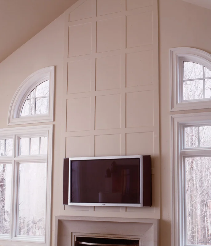 Cream-colored geometric wall paneling with mounted TV above fireplace and arched windows