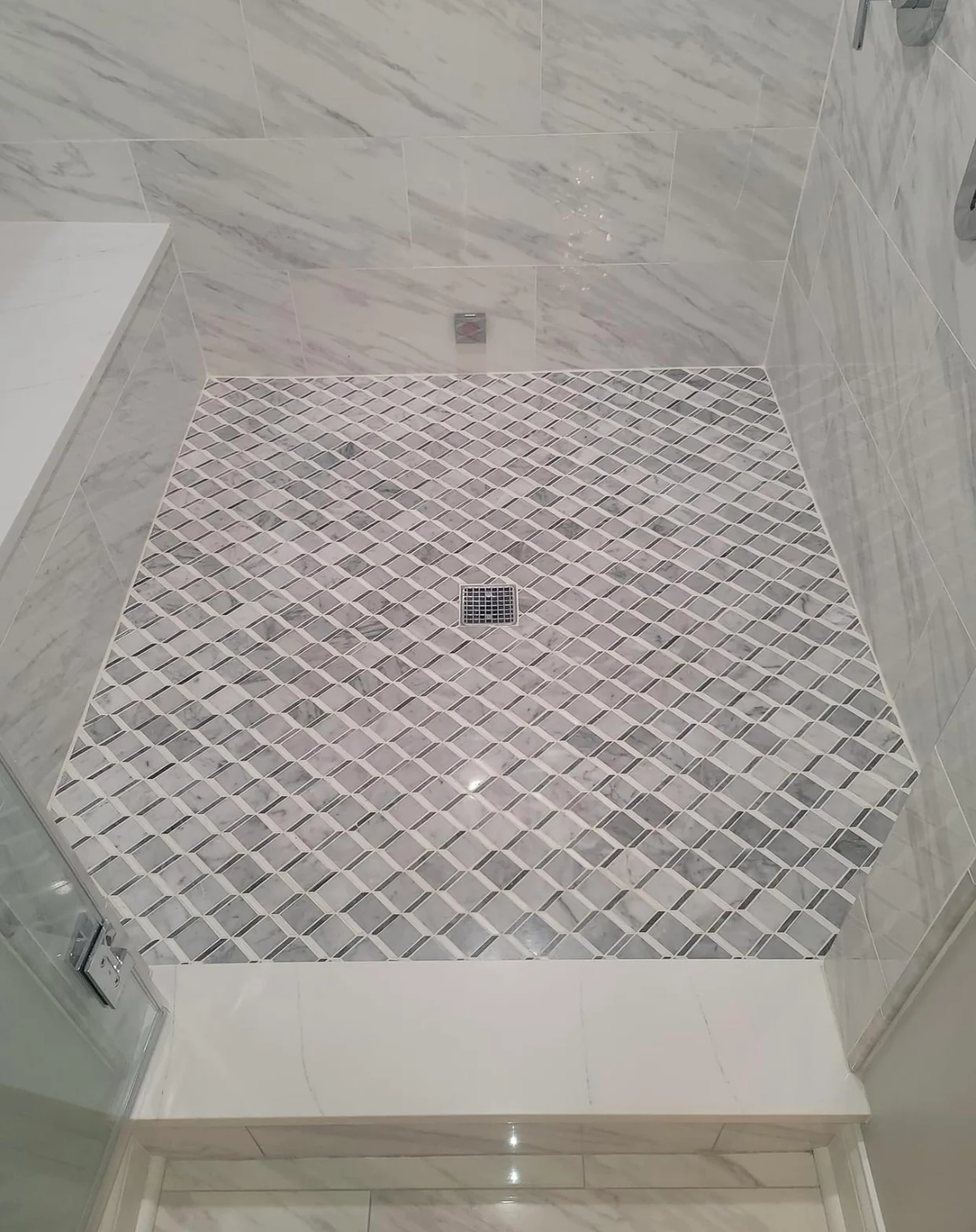 Marble tile shower with diamond pattern floor and large format wall tiles