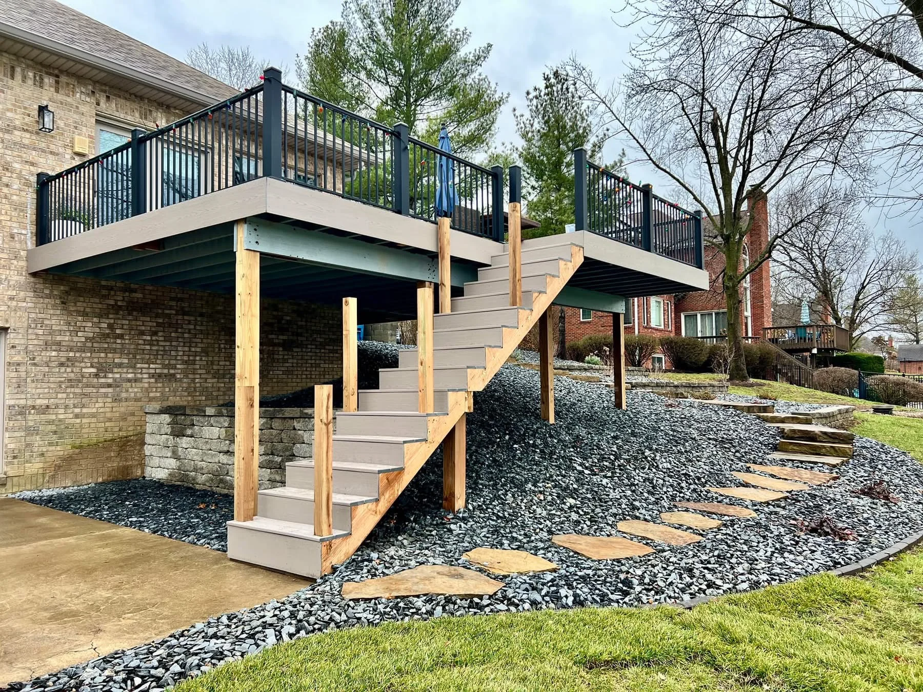 Modern elevated composite deck with black railings, timber posts, and stone landscaping