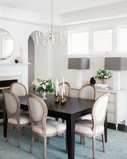 Modern dining room with black table, upholstered chairs, crystal chandelier, and custom white cabinetry