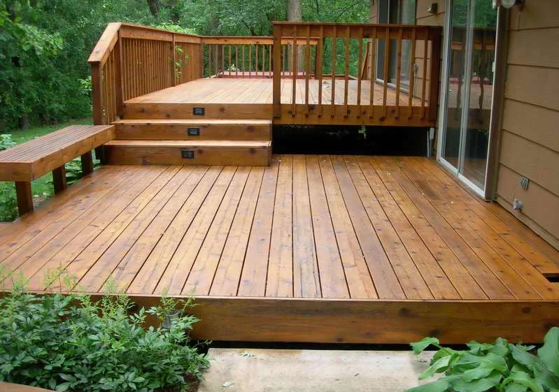 Multi-level composite deck with wooden railings and built-in seating overlooking wooded yard