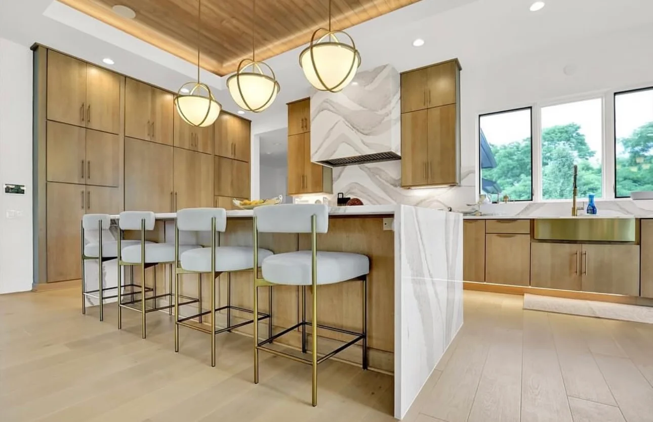 Modern kitchen with wood cabinetry, white island, marble backsplash, and pendant lighting