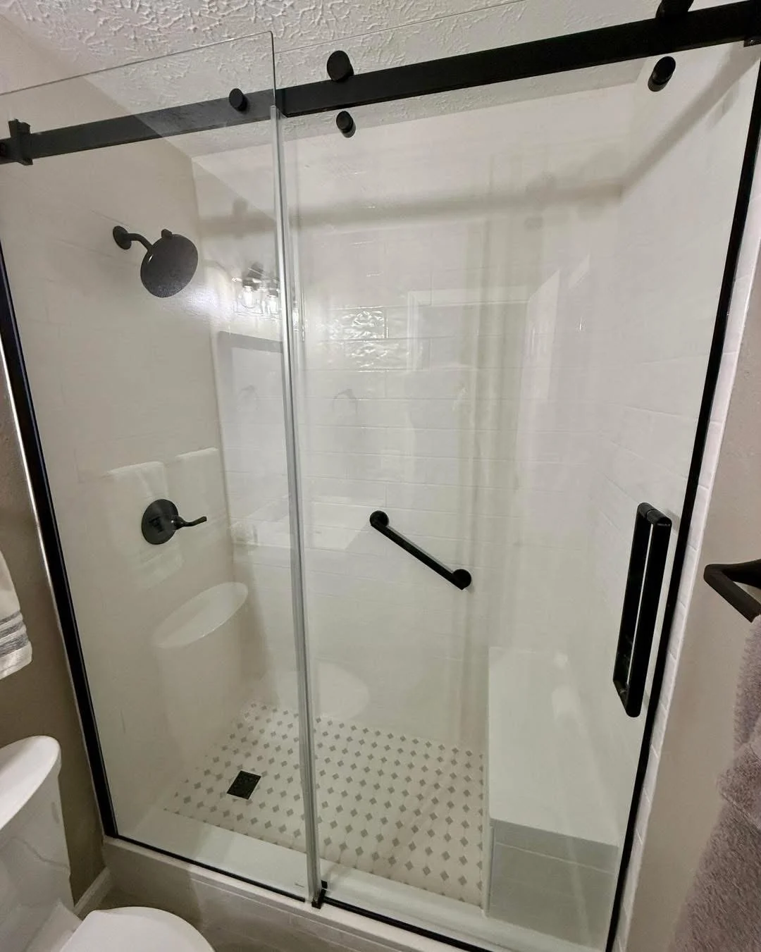 Frameless glass shower with black hardware, white tile walls, and mosaic floor