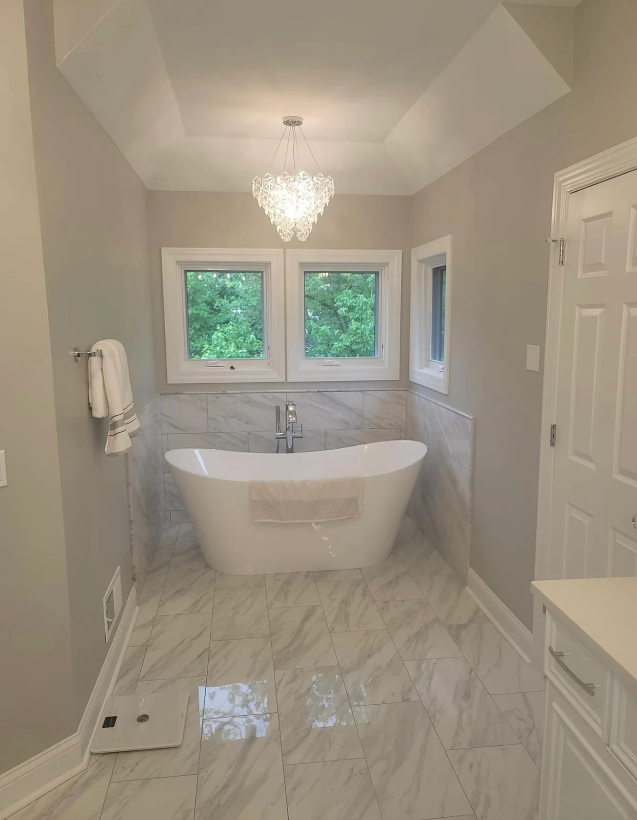 Modern master bathroom with white freestanding tub, marble tile, and dual windows