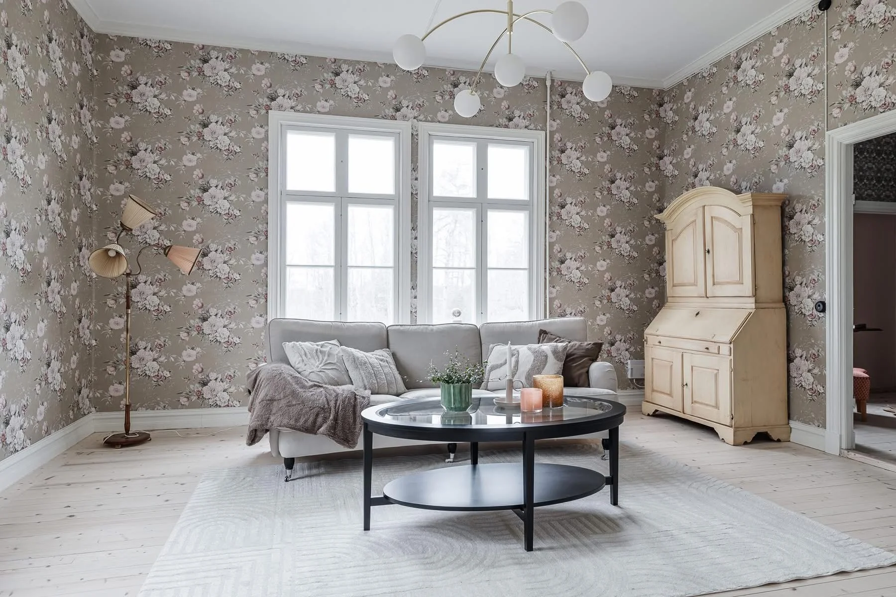 Living room with floral wallpaper, gray sofa, black round table, and cream cabinet