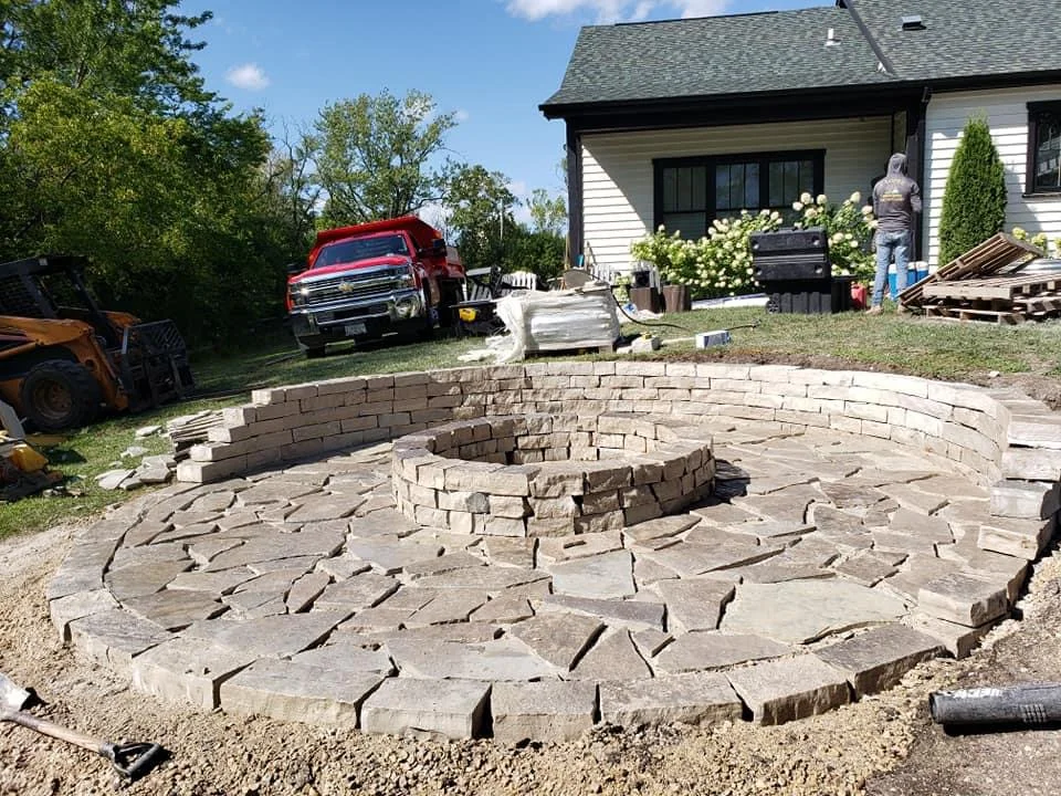 Circular stone fire pit with curved retaining wall in backyard construction phase