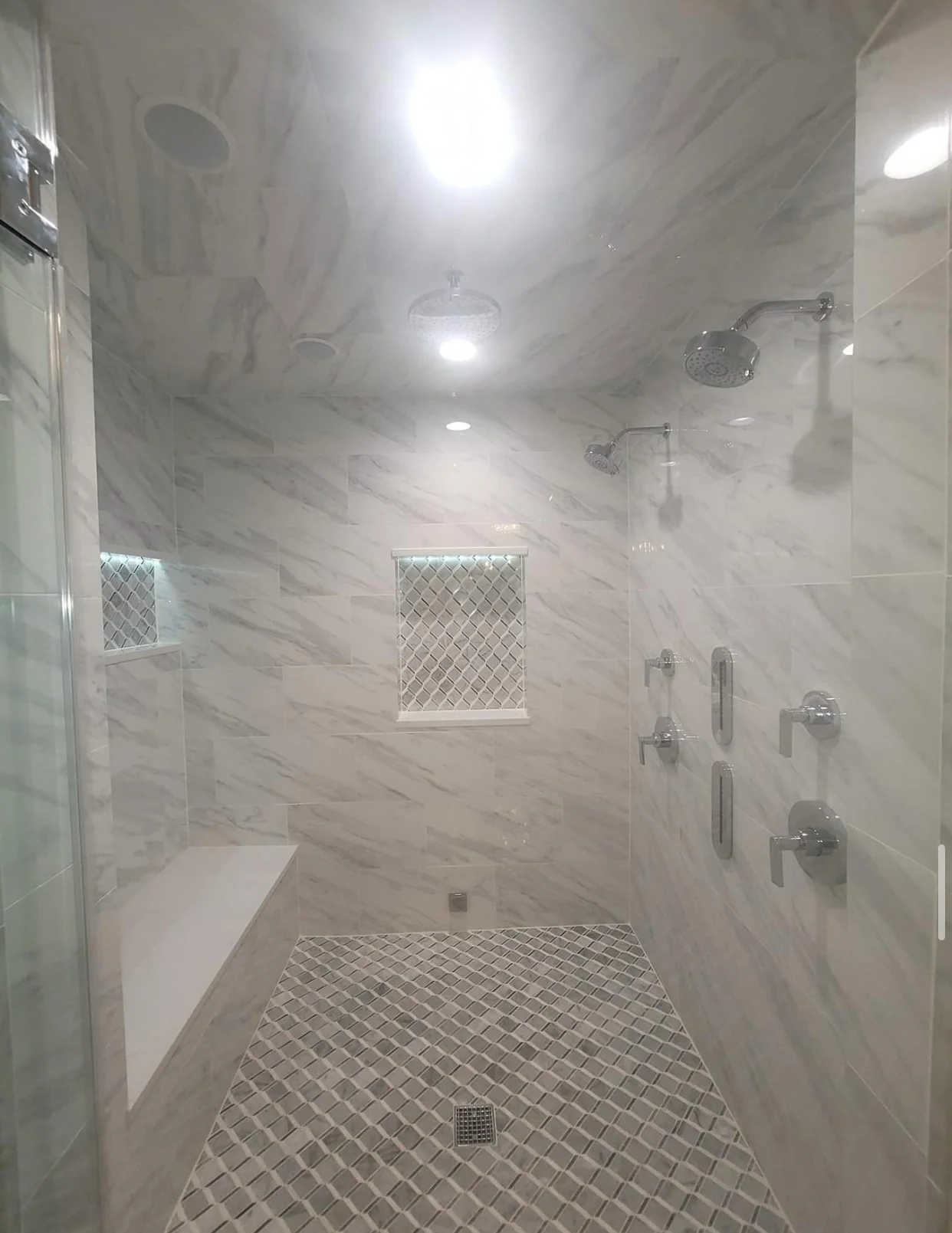 Modern bathroom with marble tile walls, dual showerheads, and geometric floor pattern