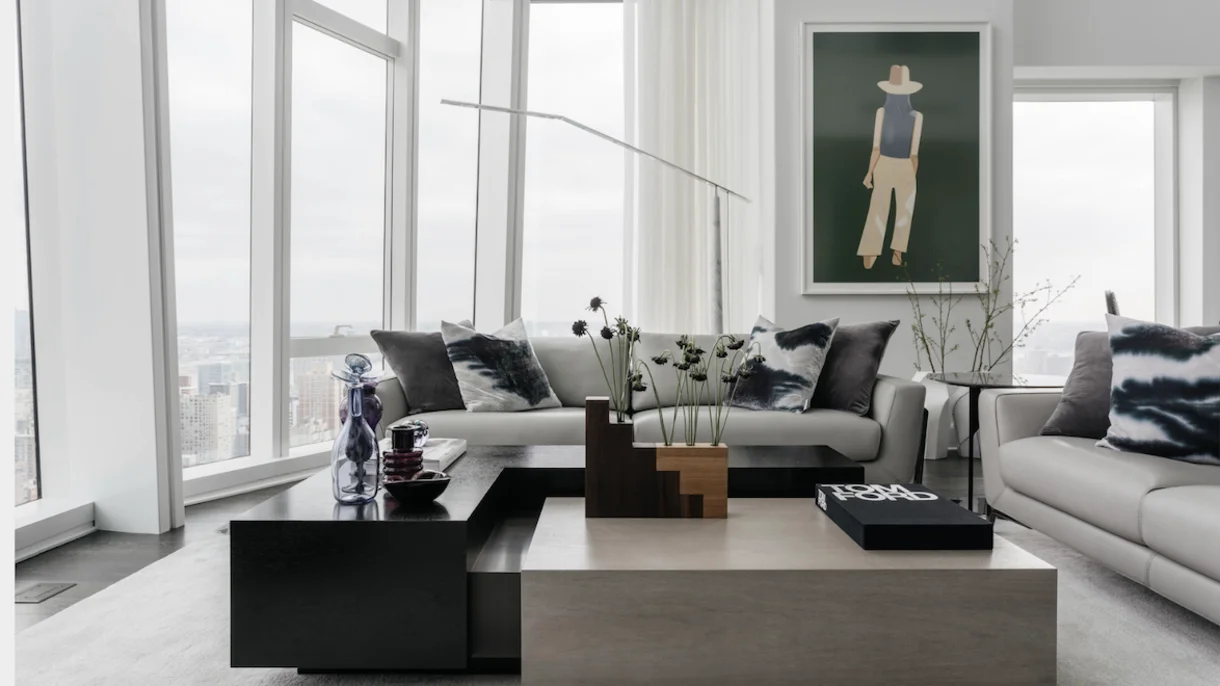 Modern living room with gray sectional, black geometric tables, and floor-to-ceiling windows overlooking city