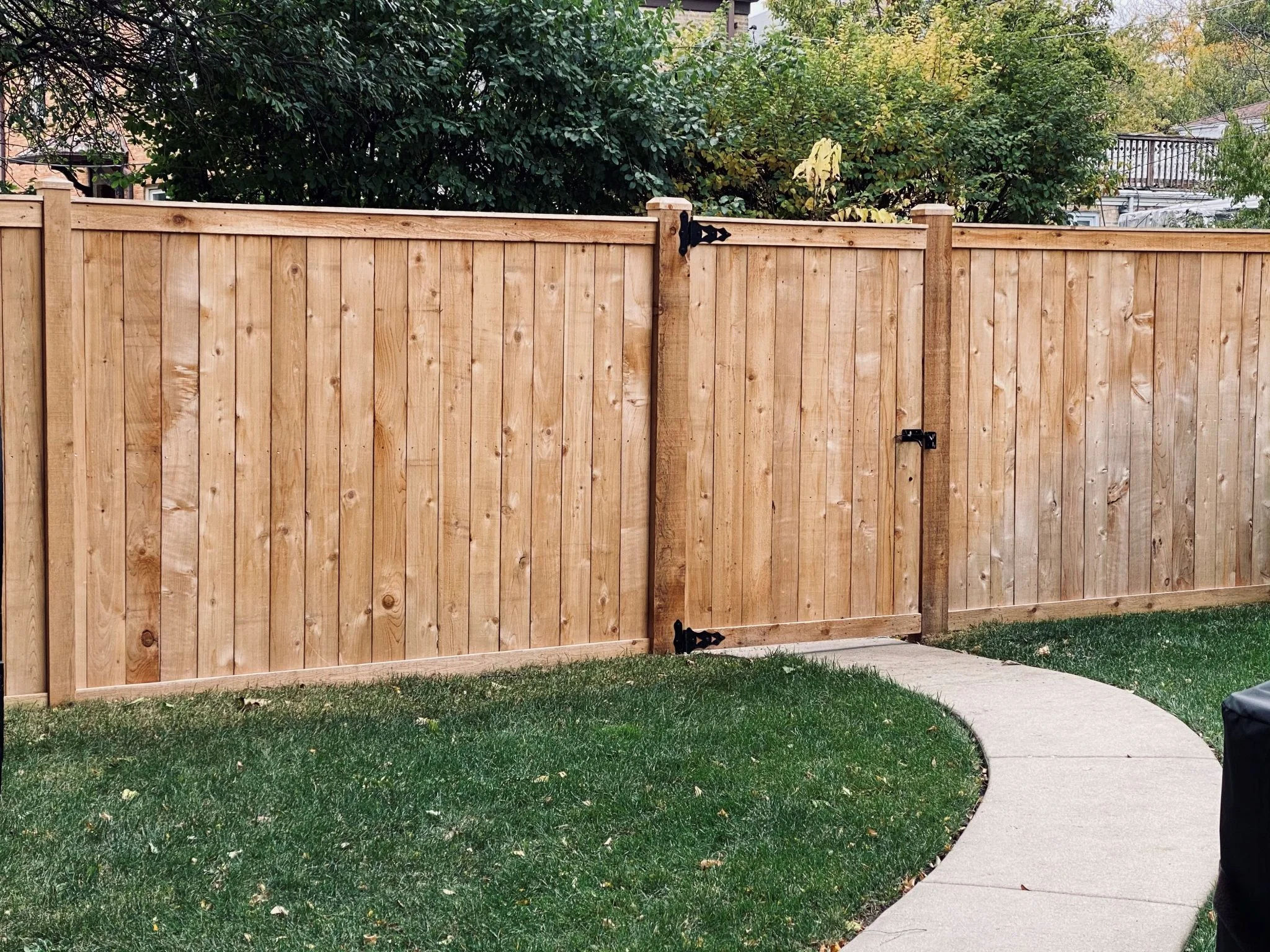 New cedar privacy fence with vertical boards and black gate hardware in backyard