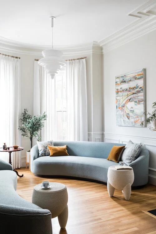 Modern living room with curved blue sofa, pendant lights, and white millwork