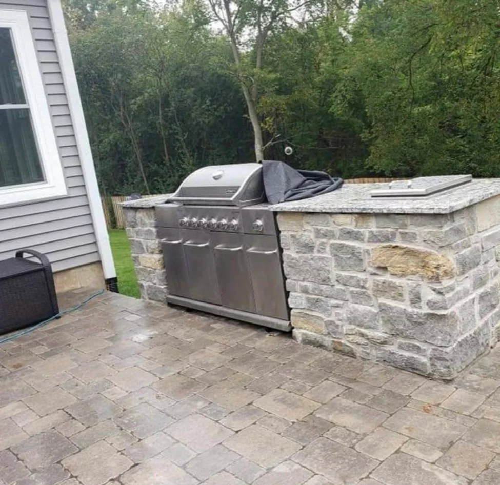 Stainless steel grill built into stone island with granite top on paver patio