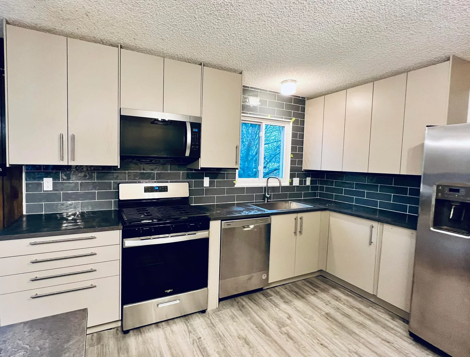 Modern kitchen with cream cabinets, dark subway tile backsplash, and stainless steel appliances