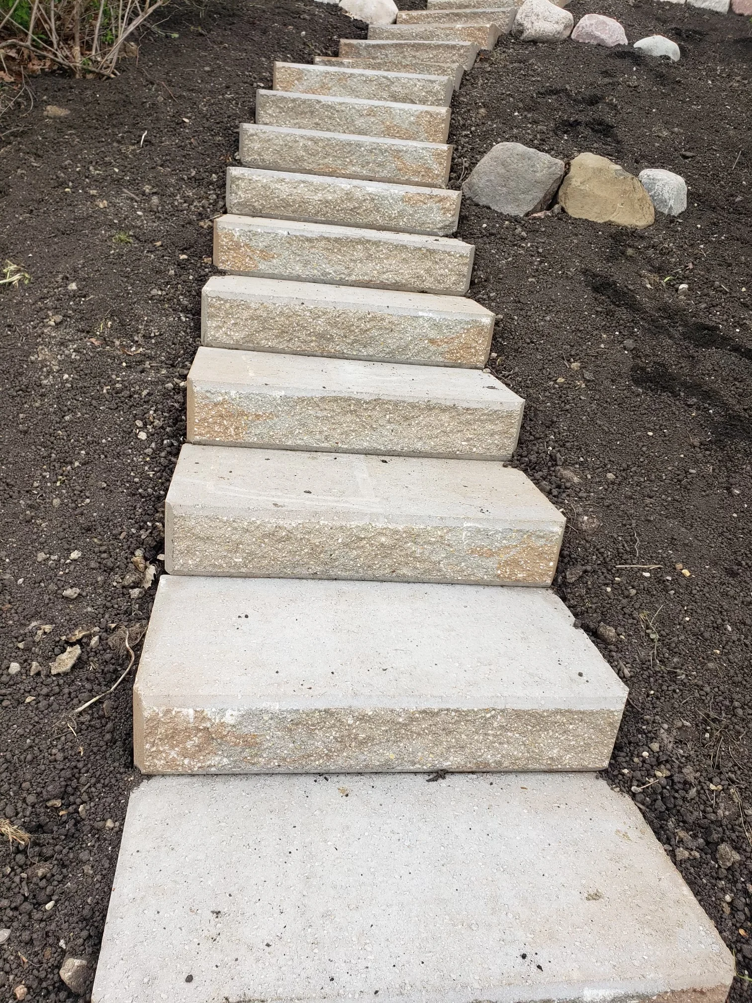 Concrete outdoor steps with alternating light and tan treads installed in landscape setting