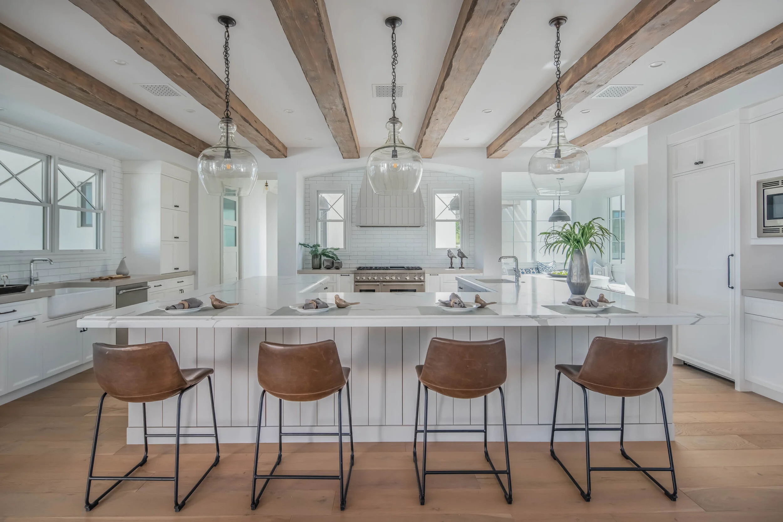 Modern farmhouse kitchen with white cabinetry, exposed beams, and large island with brown leather seating
